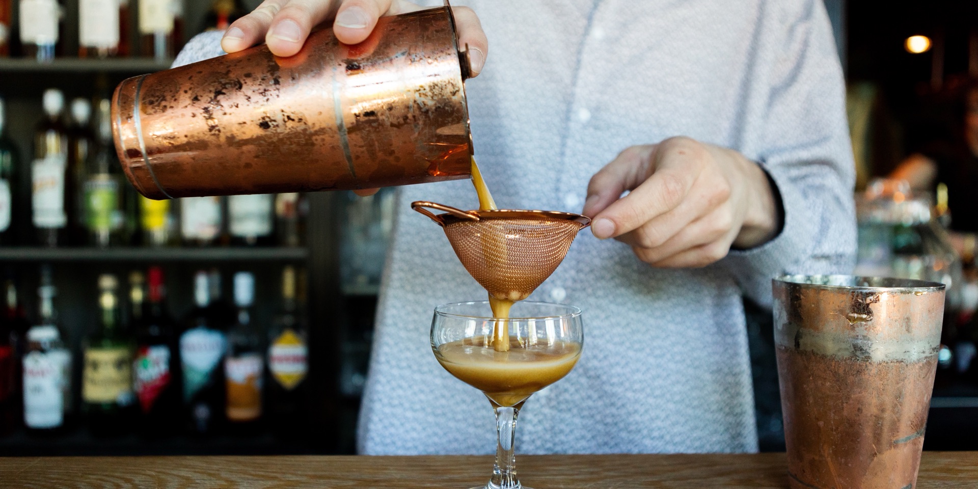 A bartender straining a cocktail into a coupe at Hopfields